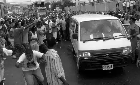 Image taken in Jamaica of a large crowd surrounding a small white van