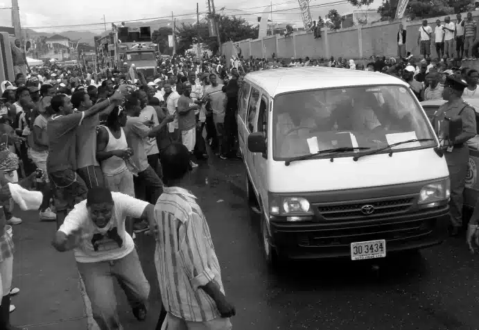 Image taken in Jamaica of a large crowd surrounding a small white van